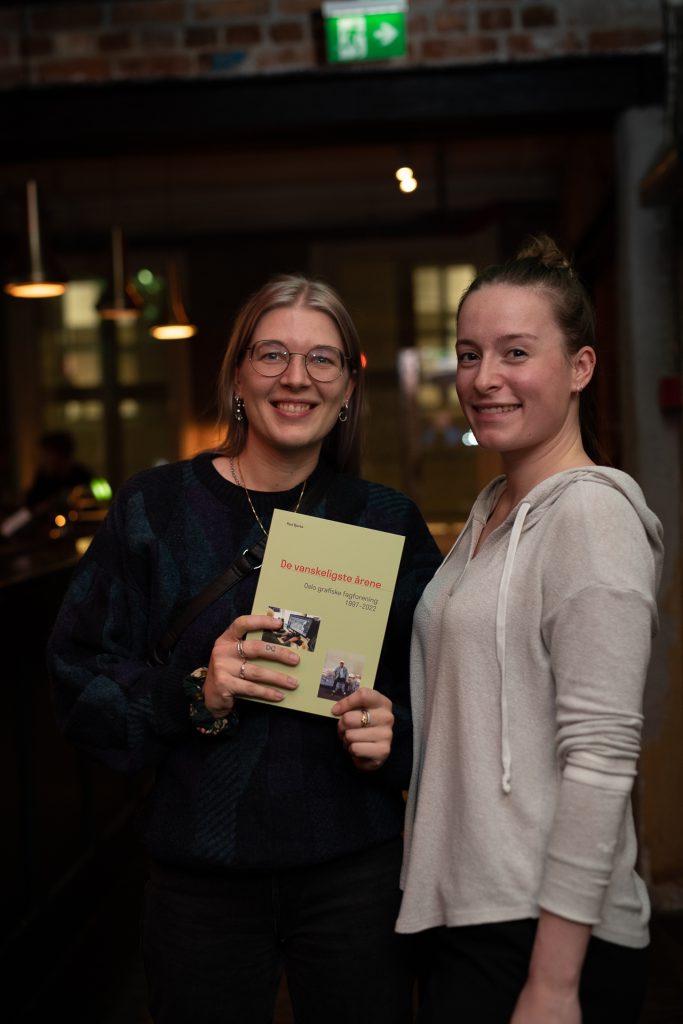 To smilende kvinner som holder boken de har designet, som handler om Ogfs siste 25 år.